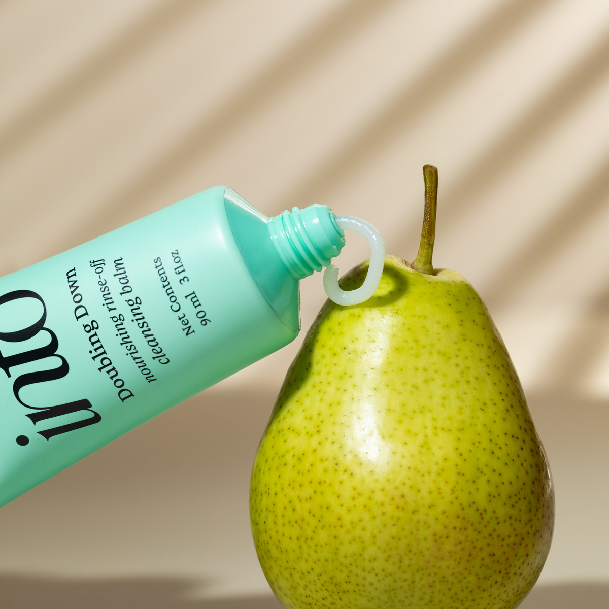 Close-up of a cleansing balm tube  on a fresh pear, highlighting the natural ingredients and nourishing qualities of the skincare product.